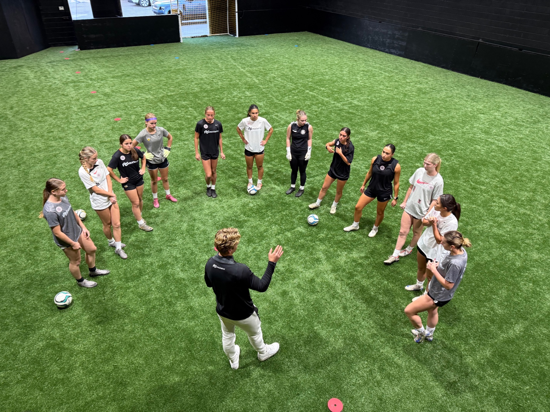 Coach leading a women's team training session on the indoor field
